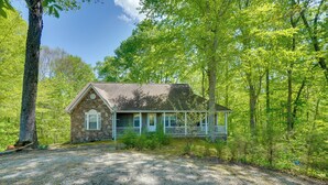 Een stenen blokhut met een veranda, omringd door bomen.
