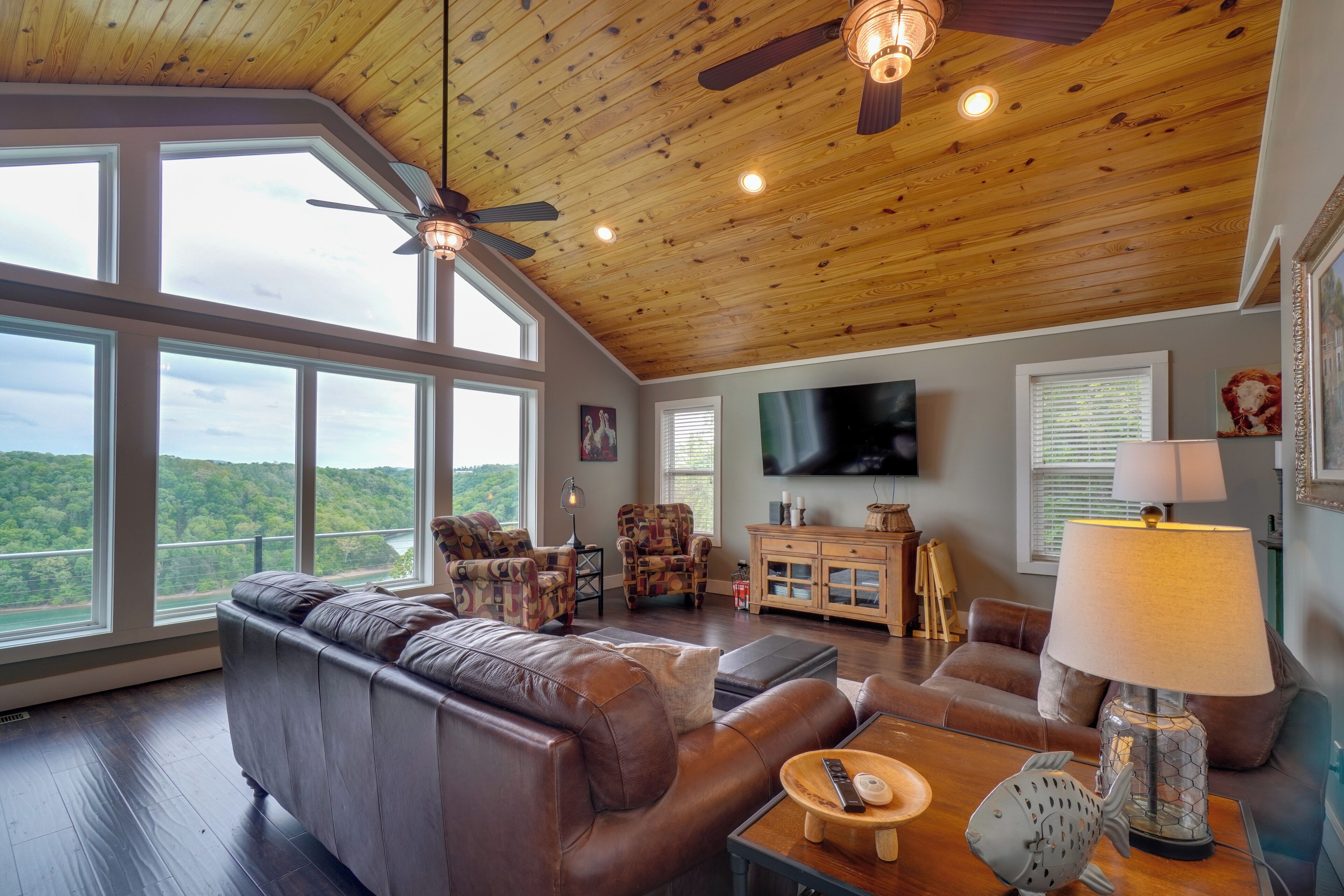 A spacious living room with a large leather sofa, a television, and a wooden ceiling with a fan.