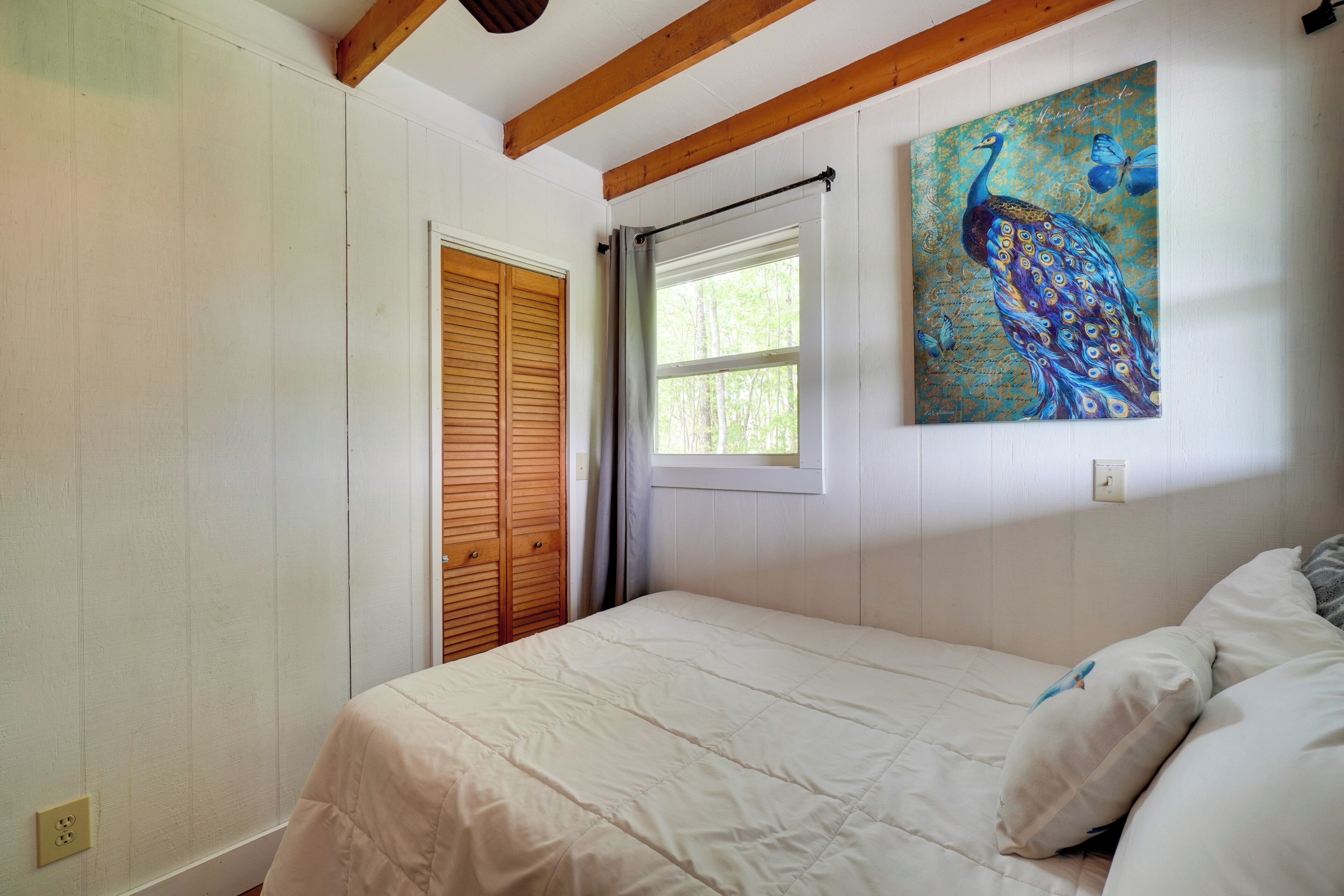 A bedroom with a bed, a window with a curtain, a wooden door, and a painting on the wall.