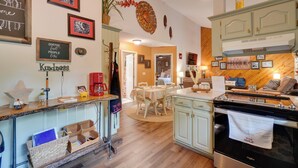 A kitchen with wooden cabinets, a stove, and a dining area with a table and chairs. - Dale Hollow Hideaway! Cabin w/ Hot Tub (Byrdstown)