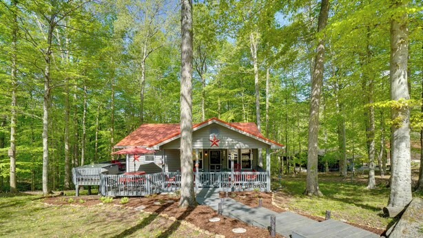 A cabin with a red roof, surrounded by trees, and a porch with outdoor seating. - Dale Hollow Hideaway! Cabin w/ Hot Tub (Byrdstown)