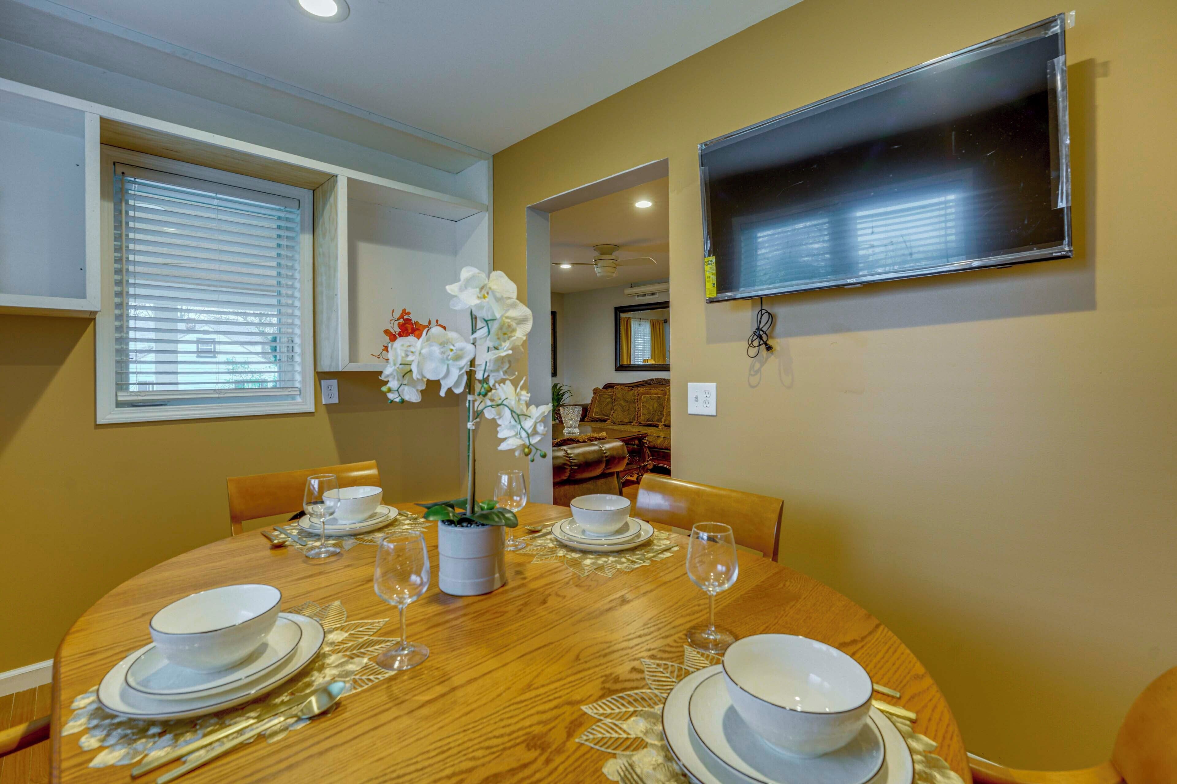 A dining area with a round table set for four, a potted plant, and a television mounted on the wall.