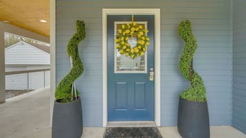 A blue door with a yellow wreath, two potted plants, and a welcome mat.