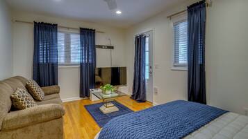 A bedroom with a bed, a sofa, a TV, and a window with curtains.
