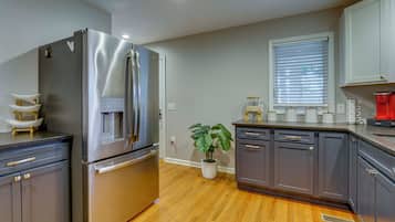 A modern kitchen with stainless steel appliances, wooden flooring, and a potted plant.