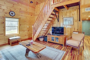 A wooden interior with a staircase, a television, a cushioned chair, and a small table. - Hike & Unwind - Quiet Wooded Getaway in Pikeville (Pikeville)