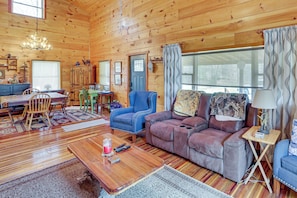 A cozy cabin interior with a wooden floor, a sofa, a dining area, and a window with curtains. - Hike & Unwind - Quiet Wooded Getaway in Pikeville (Pikeville)