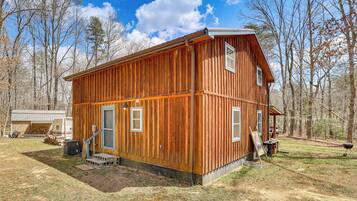 A two-story wooden cabin with a garage, a covered porch, and a grill area.