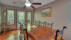 Uma sala de jantar com uma mesa de madeira, cadeiras, um ventilador de teto e um quadro na parede.