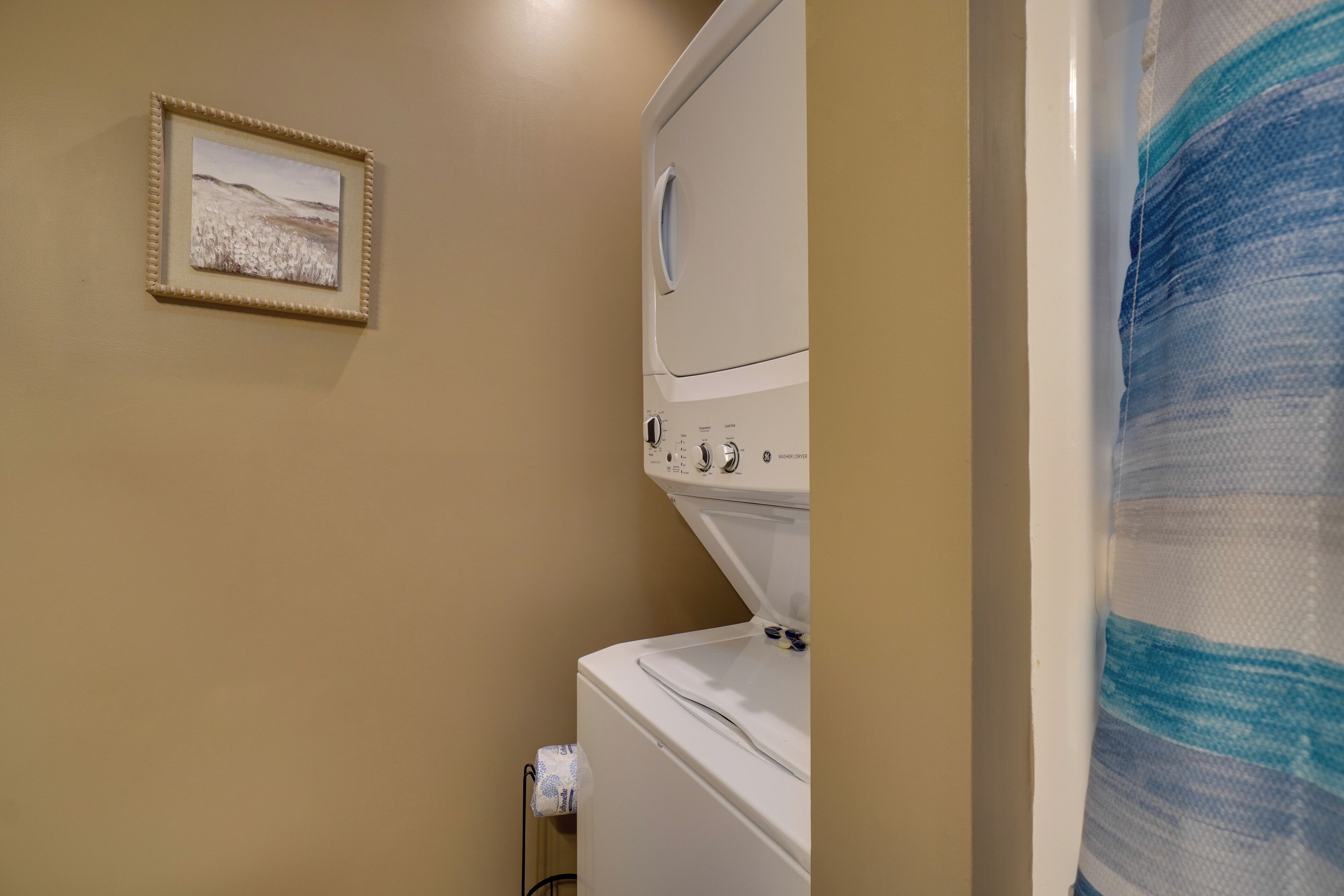 A laundry area with a washer and dryer, a towel rack, and a framed picture on the wall.