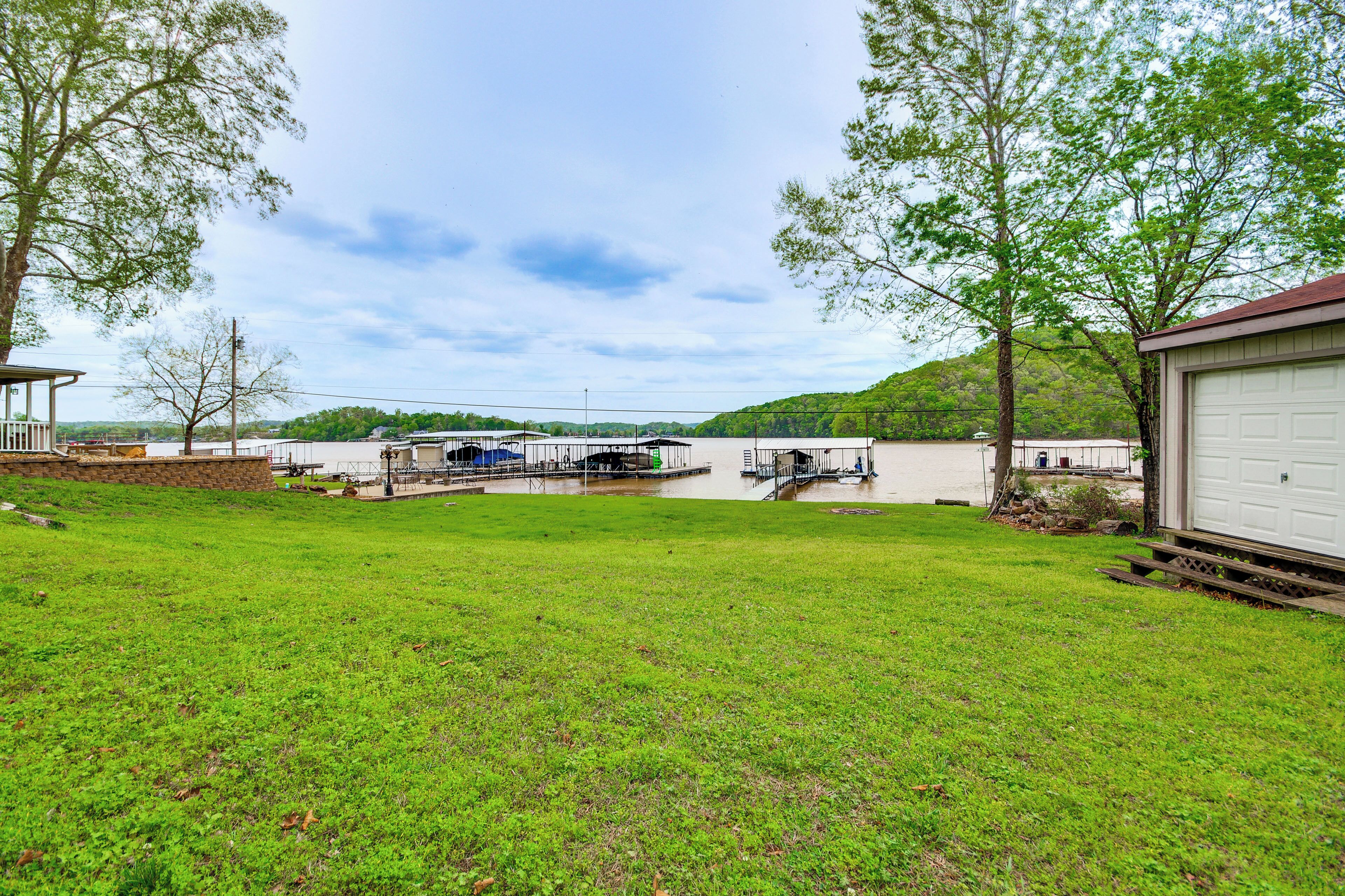 A grassy yard with a dock, a white garage, and a hill in the background.