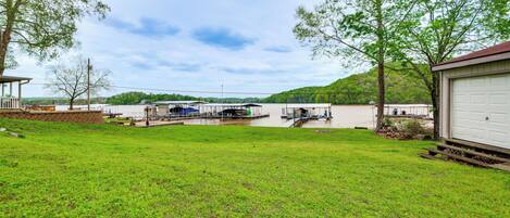 A grassy yard with a dock, a white garage, and a hill in the background.