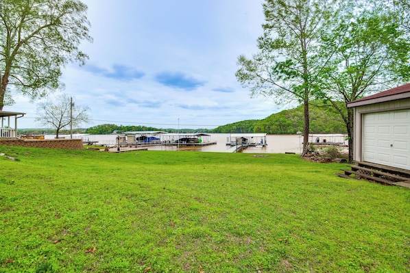 A grassy yard with a dock, a white garage, and a hill in the background.