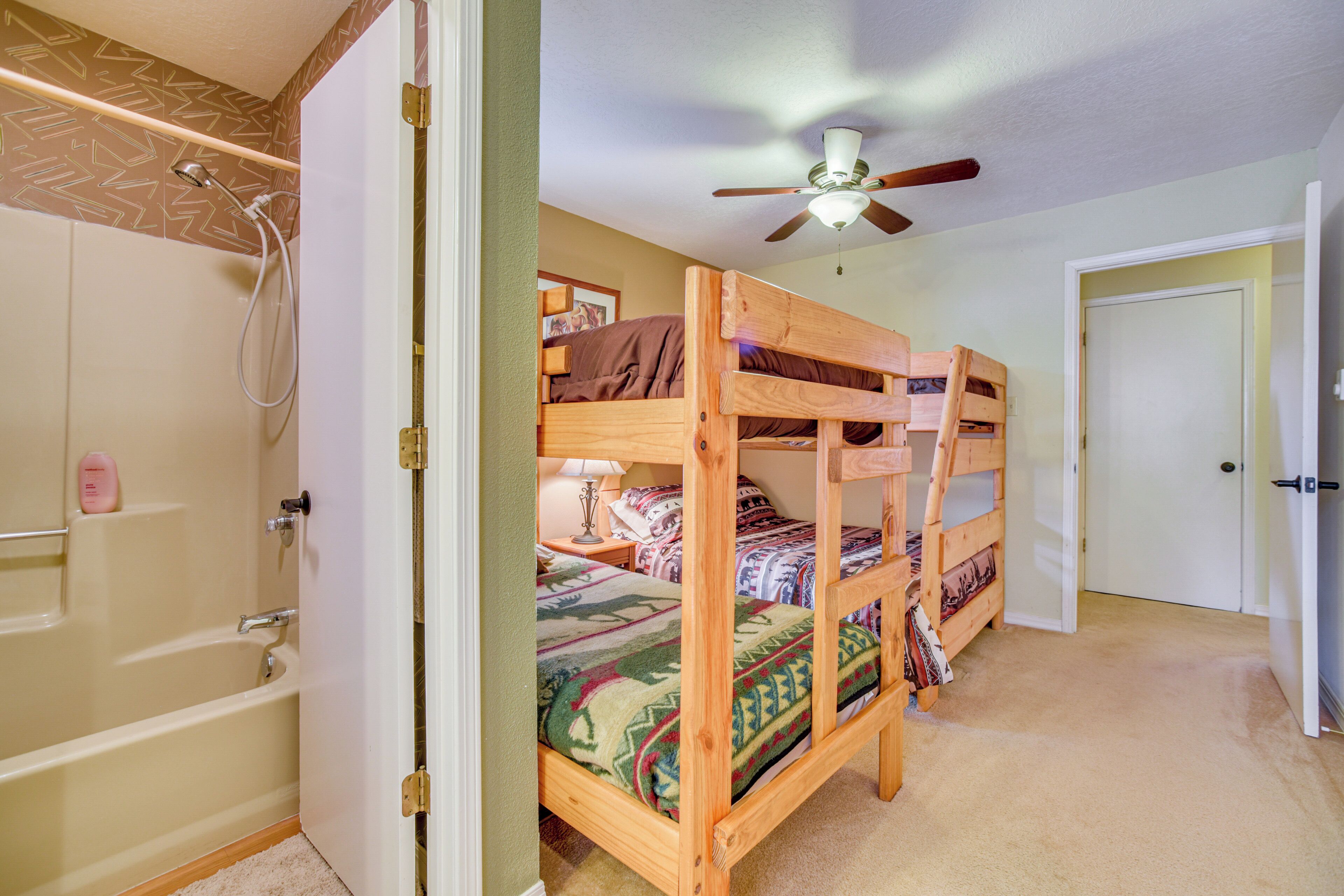 A bedroom with bunk beds, a ceiling fan, a shower, and a door leading to another room.