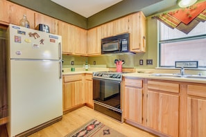A kitchen with wooden cabinets, a refrigerator, a microwave, an oven, and a window with a view. - Walk to Angel Fire Resort! Mtn-view Condo Near Fun (Angel Fire)