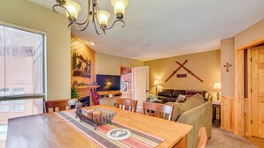 Un coin repas avec une table en bois, des chaises, un lustre et un téléviseur en arrière-plan.