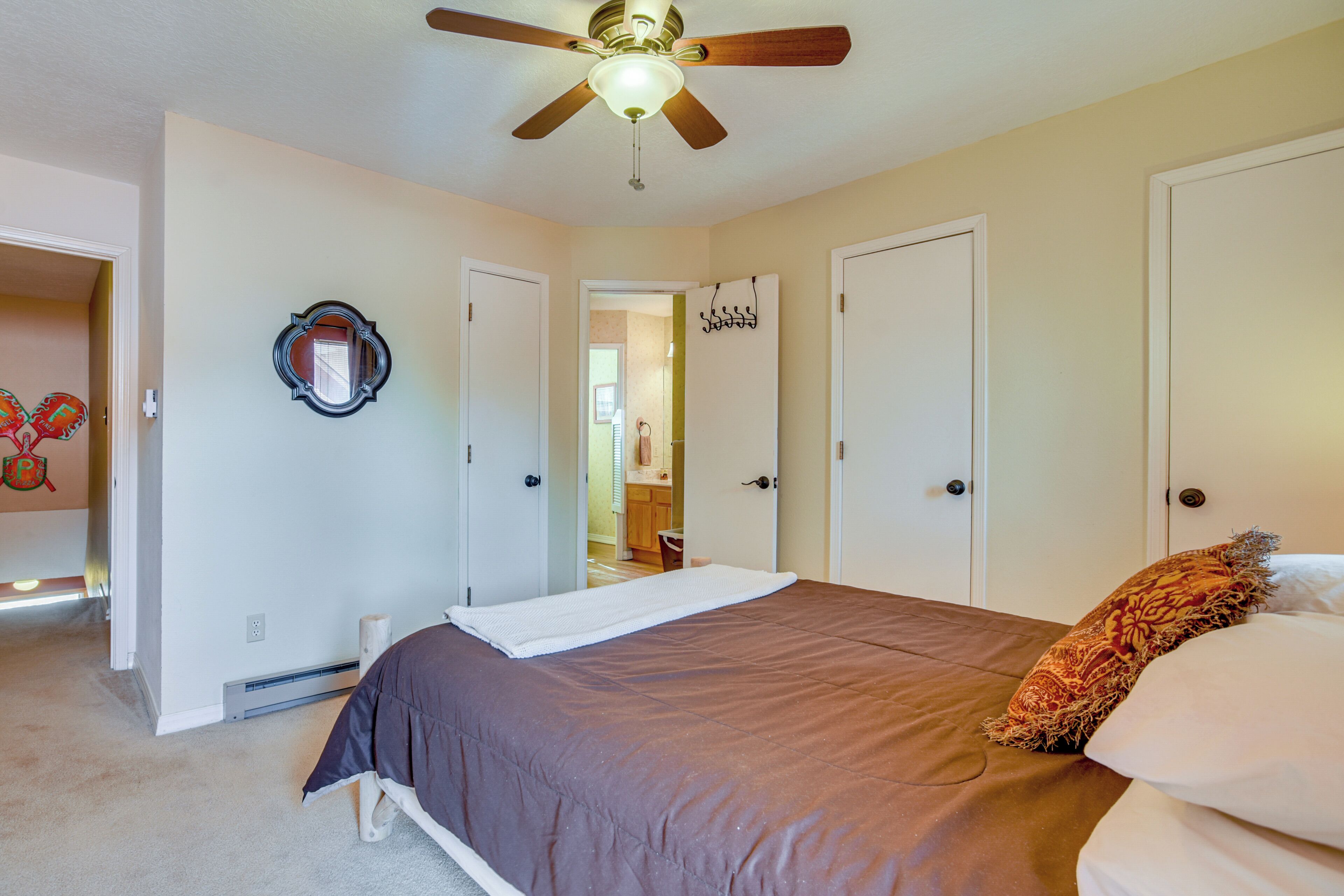 A bedroom with a bed, a ceiling fan, a mirror, and a door leading to a bathroom.