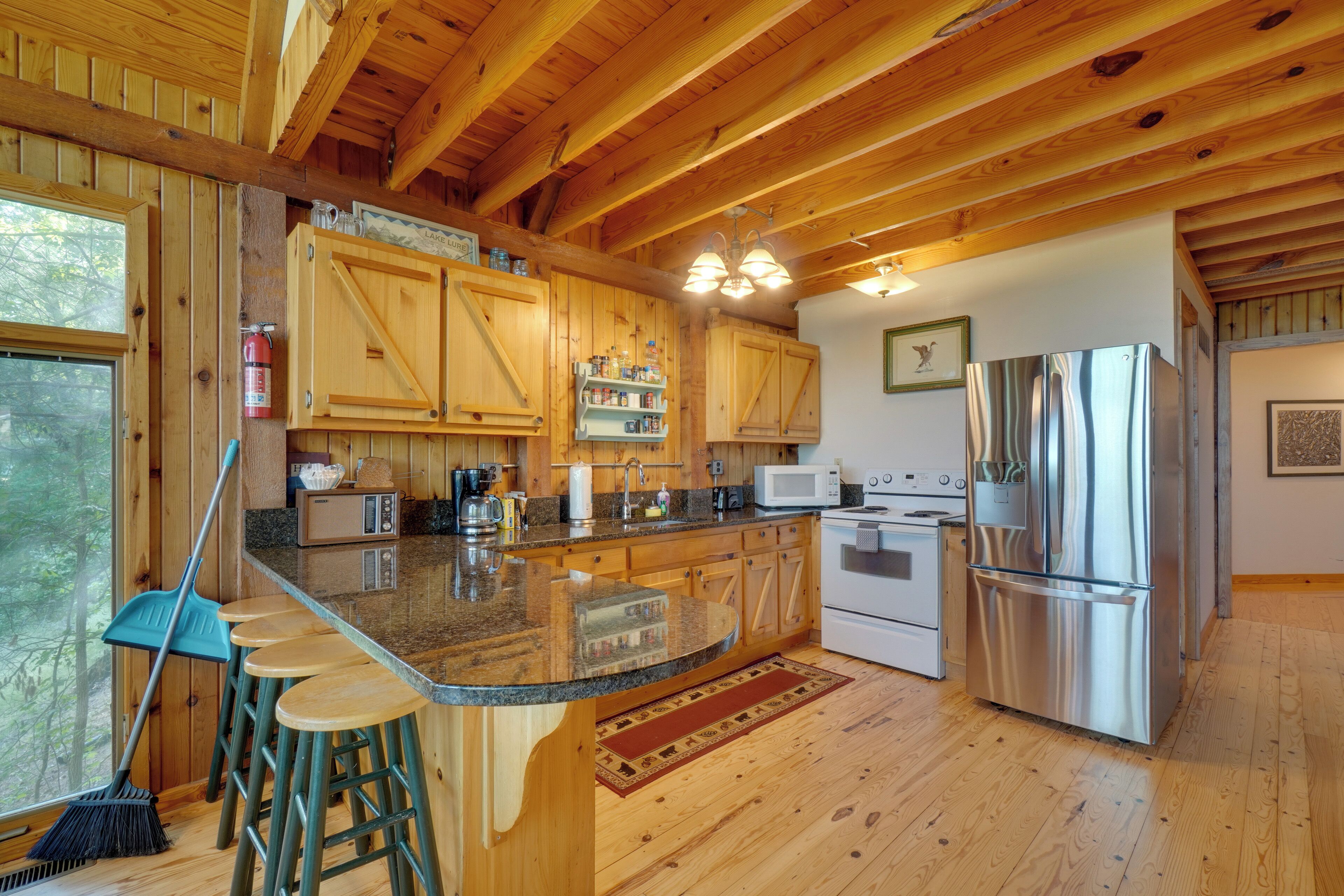 Cocina de cabaña de madera con una isla central, taburetes de bar, refrigerador, microondas, estufa y armarios de madera.