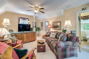A living room with a sofa, armchair, wooden cabinet, television, and a ceiling fan.