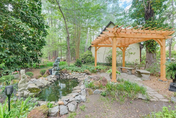 A garden with a pond, wooden pergola, and stone pathway.