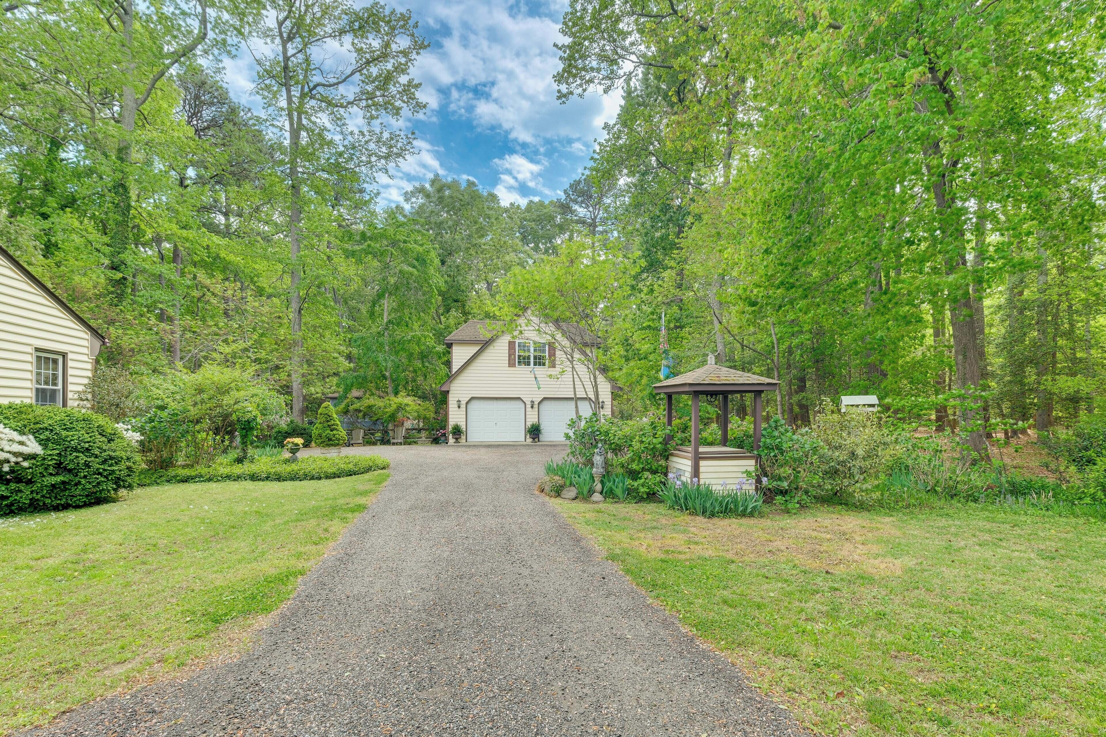 A gravel driveway leading to a house with a garage, surrounded by lush greenery and trees.