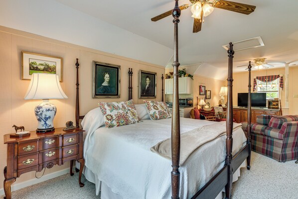 A four-poster bed with a canopy, a wooden nightstand with drawers, a lamp, and framed artwork on the wall.