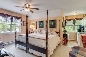 Uma cama de dossel com ventilador de teto, janela com cortinas xadrez e área de cozinha com pia e armários.