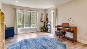 Une pièce spacieuse avec un piano, une bibliothèque, un tapis bleu et de grandes fenêtres.