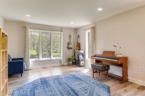 A spacious room with a piano, a bookshelf, a blue rug, and large windows.