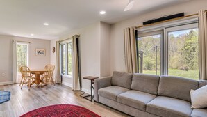 Un salon avec un canapé, une table à manger entourée de chaises, un tapis rouge et de grandes fenêtres avec des rideaux.