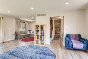 A living room with a sofa, a blue armchair, a bookshelf, and a red rug.