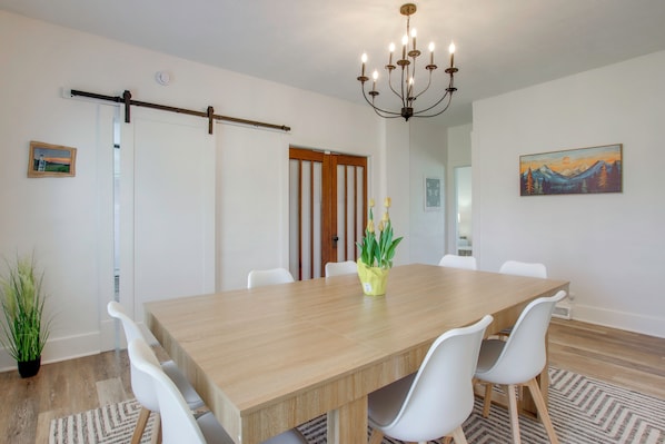 A dining area with a wooden table, white chairs, a chandelier, and a painting on the wall. - Fire Pit & Amazing Views! 15-acre Colfax Farmhouse (Colfax)
