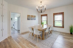 A dining area with a wooden table, white chairs, a chandelier, and artwork on the walls.
