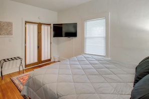 A bedroom with a bed, a television mounted on the wall, a window with blinds, and a door with a towel rack. - Fire Pit & Amazing Views! 15-acre Colfax Farmhouse (Colfax)