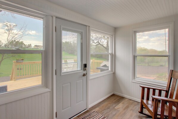 A room with a wooden floor, white walls, a door, and windows overlooking a deck.