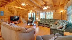 A wooden cabin interior with a sofa, a television, a ceiling fan, and a staircase. - Wooded Cabin w/ Decks & Dale Hollow Lake Views! (Byrdstown)