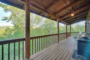 A covered outdoor deck with a grill, wooden railings, and a view of a forested area. - Wooded Cabin w/ Decks & Dale Hollow Lake Views! (Byrdstown)