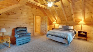 A cozy bedroom with a bed, a chair, a ceiling fan, and a nightstand with lamps. - Wooded Cabin w/ Decks & Dale Hollow Lake Views! (Byrdstown)