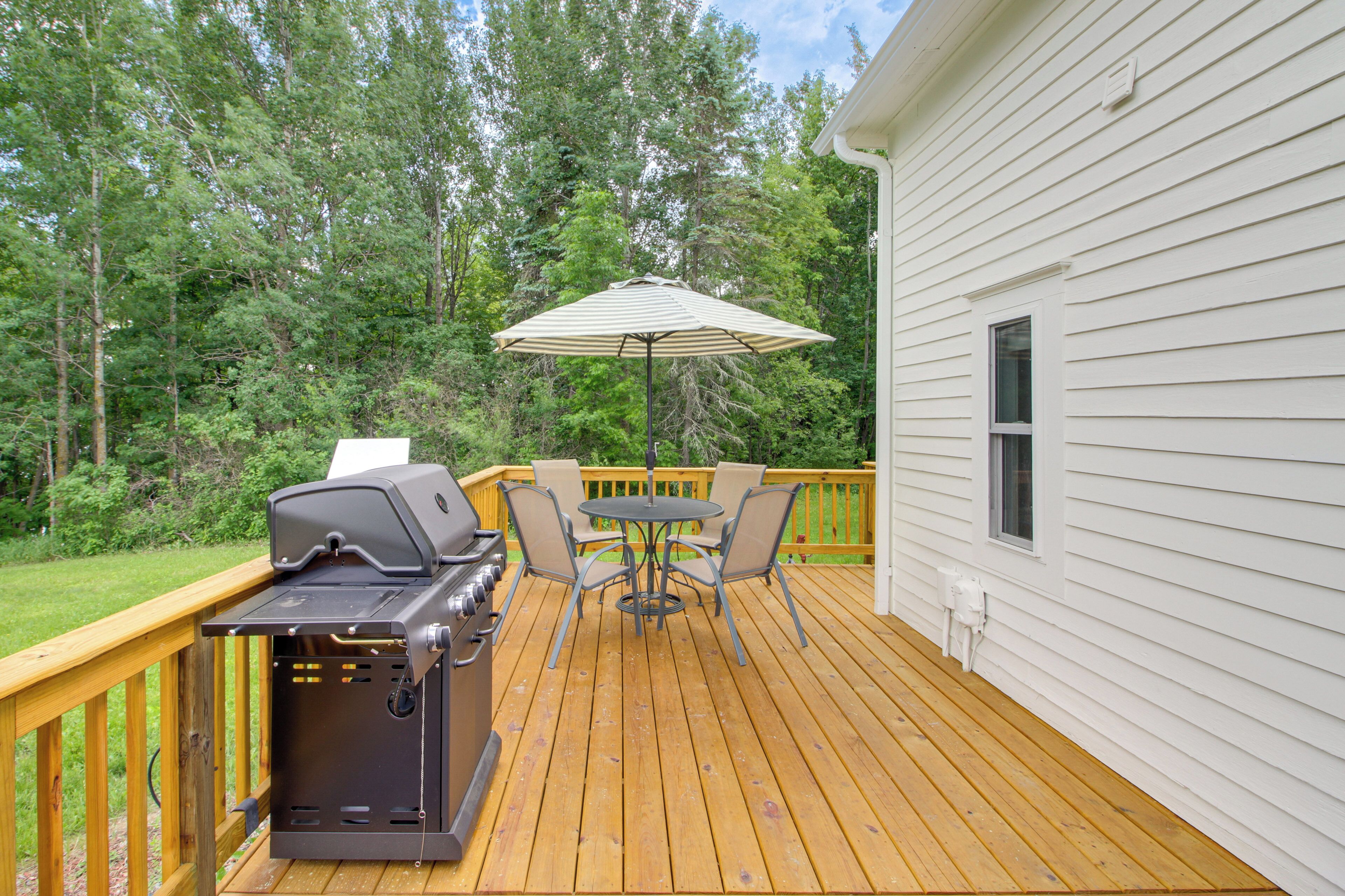 A deck with a grill, outdoor table, chairs, and an umbrella.