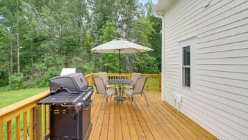 A deck with a grill, outdoor table, chairs, and an umbrella.