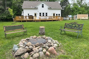 A white house with a deck, two benches, and a stone fire pit. - Lake Country House on 11th Crow Wing Lake w/ Dock (Akeley)