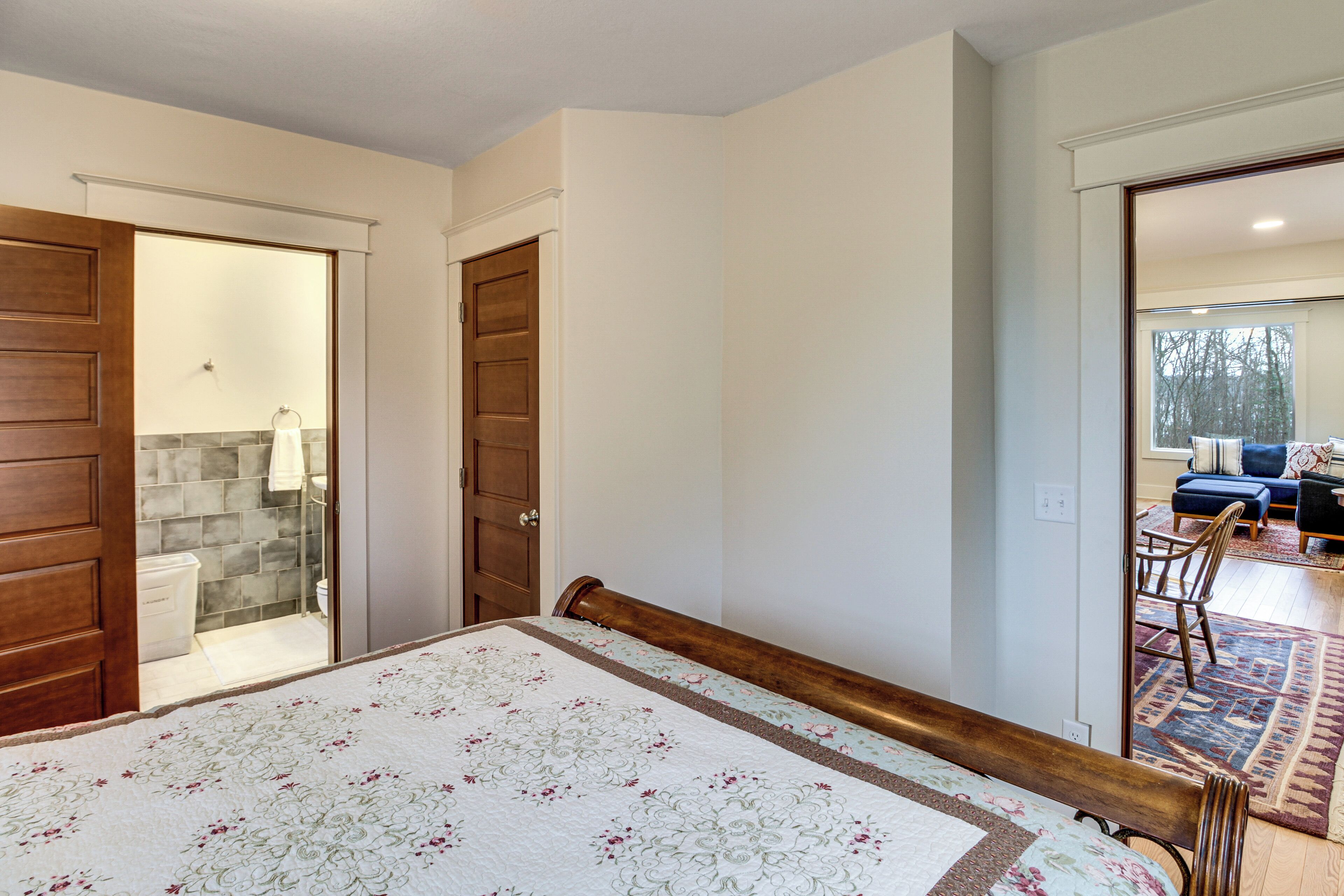 A bedroom with a bed, wooden door, and a view of a living area through an open door.