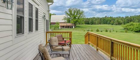 A wooden deck with outdoor furniture, a railing, and a view of a green landscape.