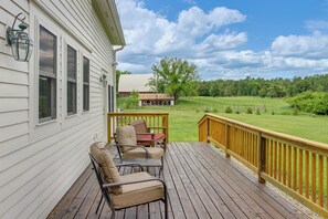 Um deck de madeira com móveis de exterior, guarda-corpo e vista para uma paisagem verde.