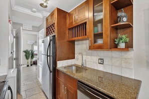 A kitchen with wooden cabinets, granite countertops, a stainless steel refrigerator, and a built-in sink.
