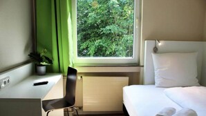 A hotel room with a bed, a desk, a chair, a window with a view of trees, and a radiator. - 2 Person Holiday Park Home in Bendorf (Bendorf)