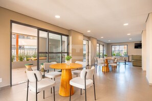 Amplo espaço interno com uma mesa redonda de madeira cercada por cadeiras, janelas grandes e uma varanda visível.