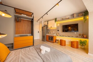 A modern hotel room with a bed, a desk, a kitchenette, and a TV. - Hospedez - Estudios Campo Belo Movi (São Paulo)