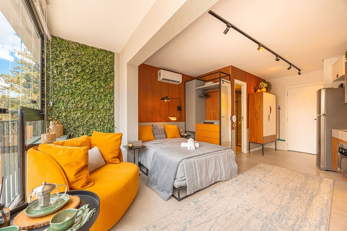 A modern bedroom with a bed, a sofa, a desk, and a kitchen area.