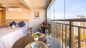 A hotel room with a bed, a small table with a vase and wine glass, and a balcony with a city view. - Hospedez - Estudios Campo Belo Movi (São Paulo)